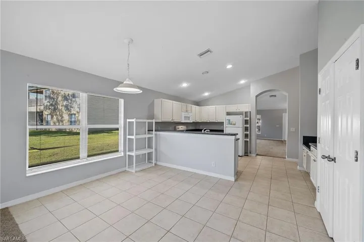 Kitchen featuring dark countertops, arched walkways, a peninsula, lofted ceiling, and hanging light fixtures