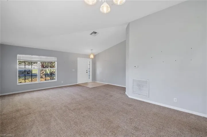 Carpeted empty room featuring vaulted ceiling and a chandelier