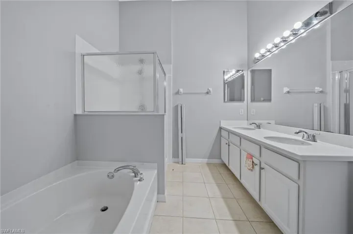 Bathroom featuring a garden tub, double vanity, light tile patterned floors, and a stall shower