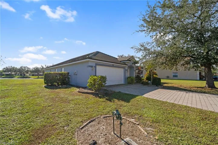 View of side of home with stucco siding, a lawn, a garage, and decorative driveway