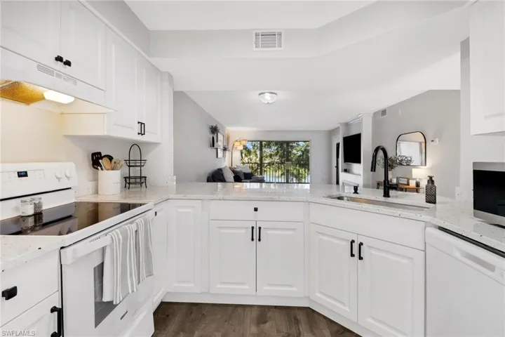 Kitchen with kitchen peninsula, white appliances, white cabinetry, and sink