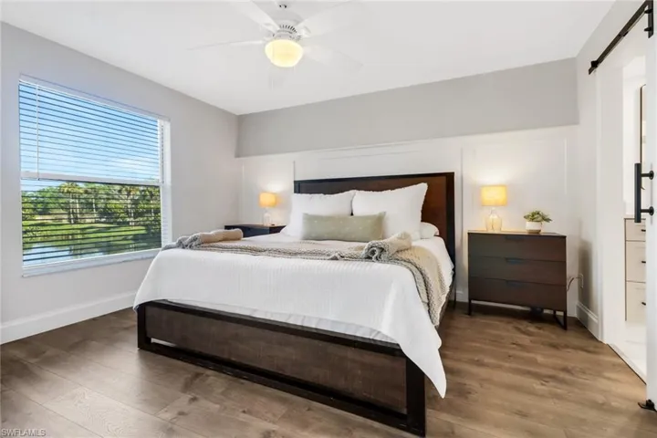 Bedroom featuring dark hardwood / wood-style flooring, a barn door, and ceiling fan