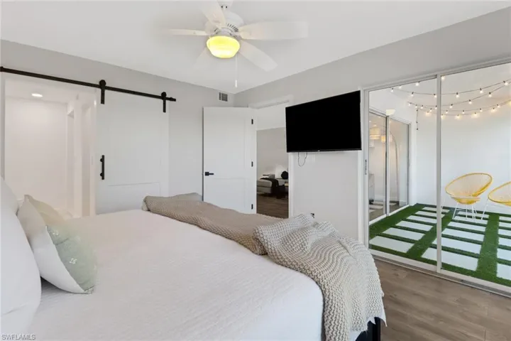 Bedroom featuring access to exterior, wood-type flooring, a barn door, and ceiling fan
