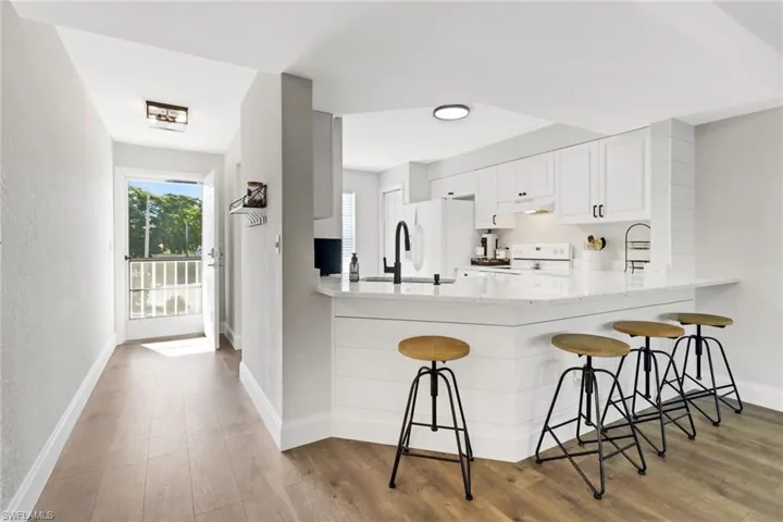 Kitchen with a kitchen breakfast bar, kitchen peninsula, white appliances, white cabinets, and hardwood / wood-style flooring