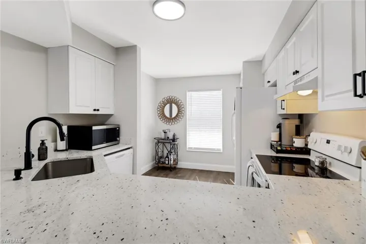 Kitchen with white appliances, white cabinets, sink, light wood-type flooring, and light stone counters