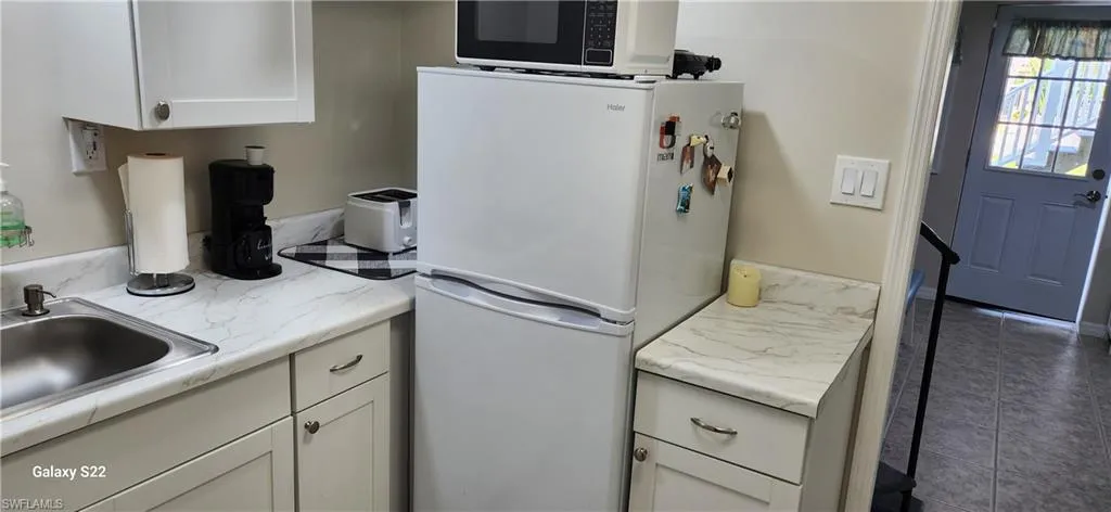 Kitchen featuring dark tile patterned flooring, sink, white fridge, and white cabinetry