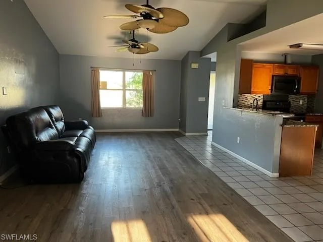 Living area featuring a ceiling fan, baseboards, vaulted ceiling, and wood finished floors