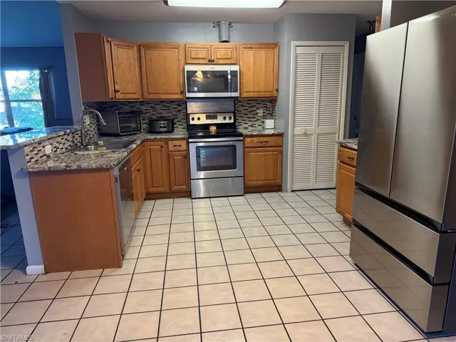 Kitchen featuring sink, light tile patterned floors, dark stone countertops, stainless steel appliances, and tasteful backsplash