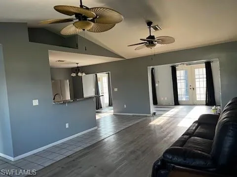Living room with ceiling fan with notable chandelier, french doors, vaulted ceiling, and wood finished floors