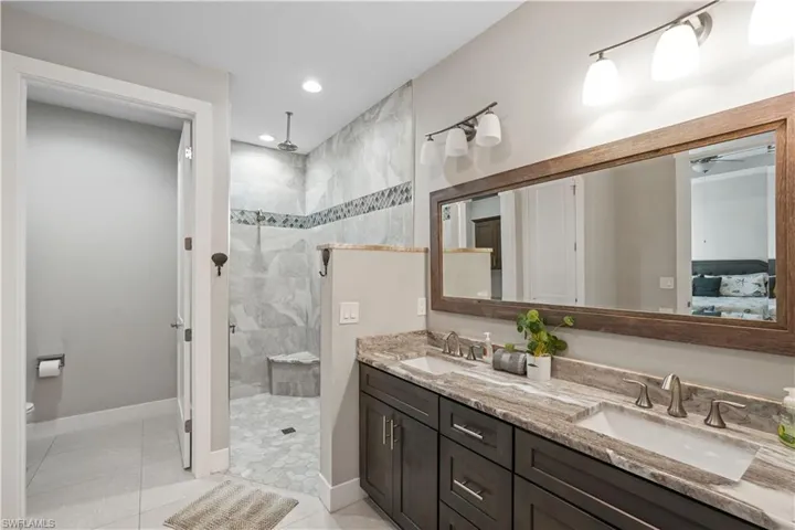 Full bath featuring a walk in shower, double vanity, ensuite bathroom, light tile patterned floors, and recessed lighting