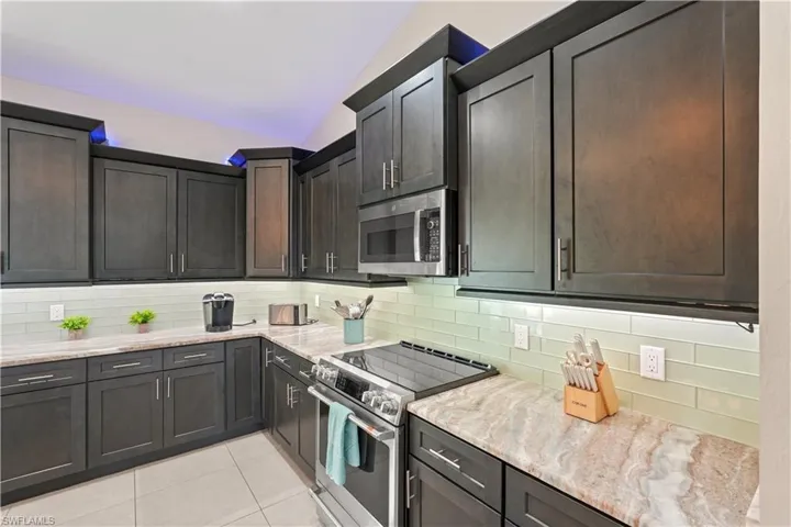 Kitchen featuring lofted ceiling, stainless steel appliances, light stone countertops, backsplash, and light tile patterned floors