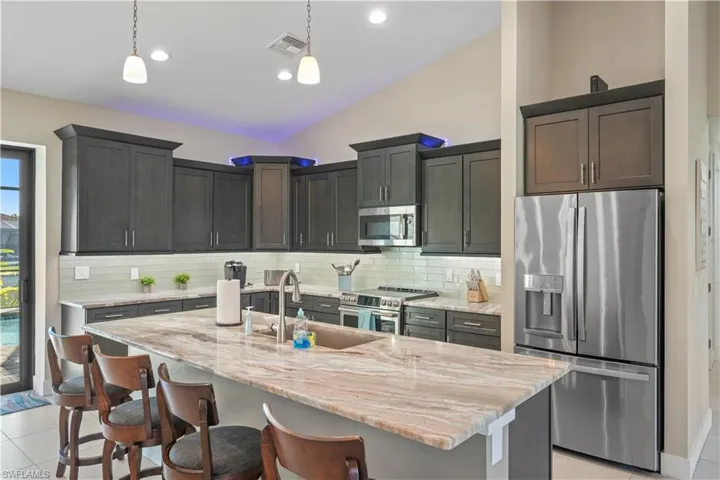Kitchen featuring stainless steel appliances, light stone countertops, light tile patterned floors, a kitchen island with sink, and lofted ceiling