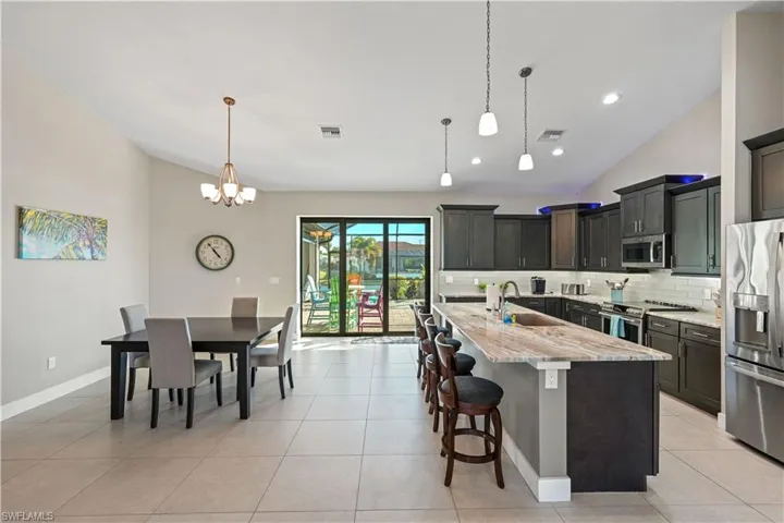 Kitchen featuring lofted ceiling, stainless steel appliances, a kitchen breakfast bar, light stone countertops, and an island with sink