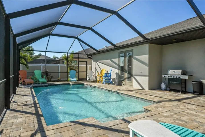 View of pool with patio surround, glass enclosure, a sunroom, and area for grilling