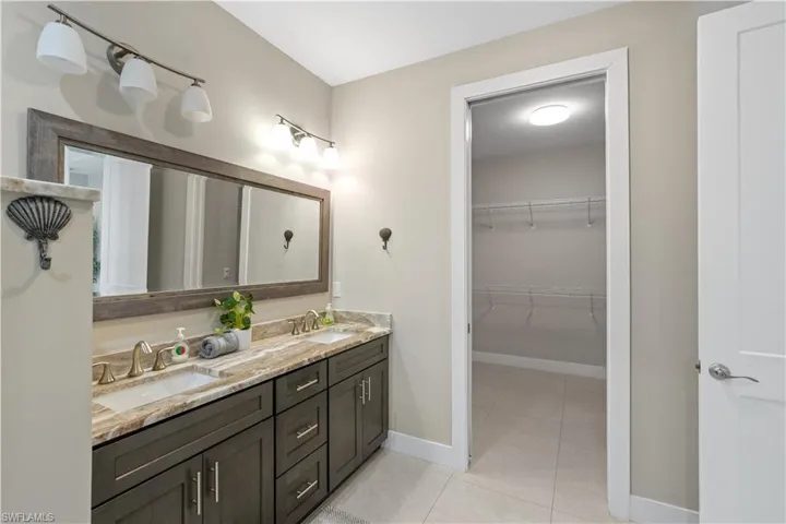 Full bath with double vanity, light tile patterned floors, and a spacious closet