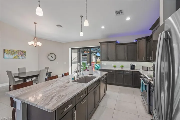 Kitchen featuring stainless steel appliances, dark wood finish cabinetry, a center island with sink, and a kitchen bar