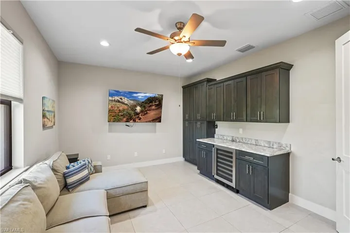 Bar with wine cooler, a ceiling fan, recessed lighting, light stone counters, and dark cabinetry