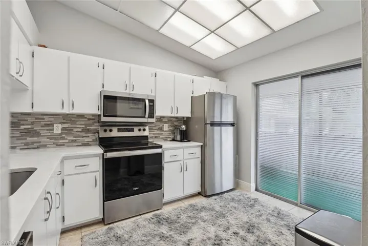 Kitchen with appliances with stainless steel finishes, light countertops, decorative backsplash, white cabinetry, and lofted ceiling