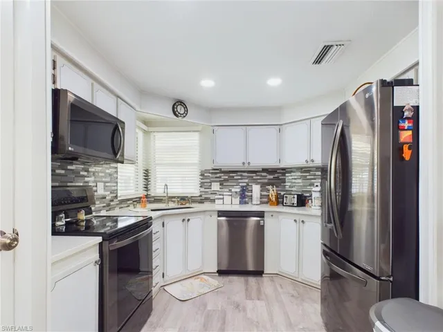Kitchen featuring appliances with stainless steel finishes, sink, light hardwood / wood-style flooring, and decorative backsplash