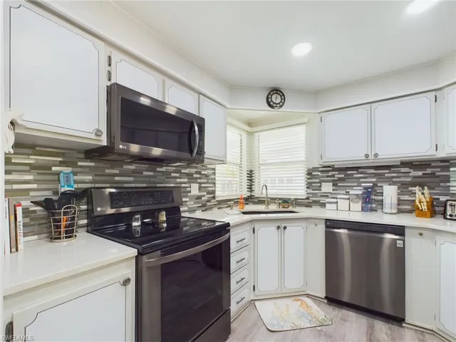 Kitchen with appliances with stainless steel finishes, light hardwood / wood-style flooring, sink, and white cabinetry