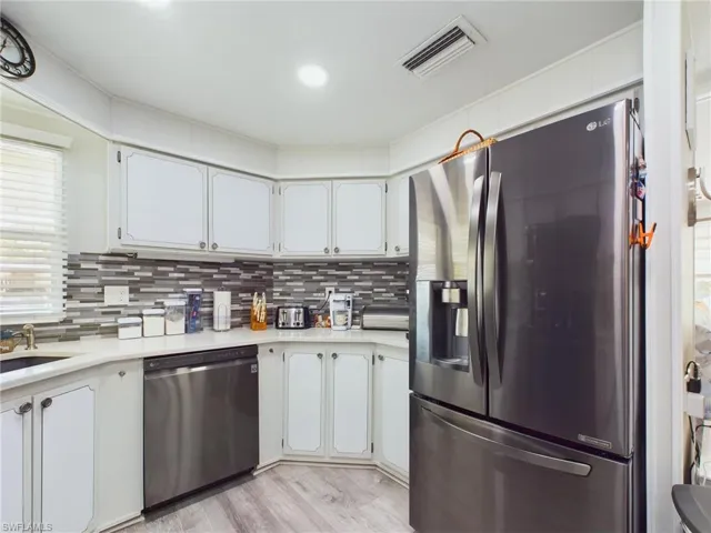 Kitchen with stainless steel appliances, white cabinetry, light hardwood / wood-style floors, tasteful backsplash, and sink