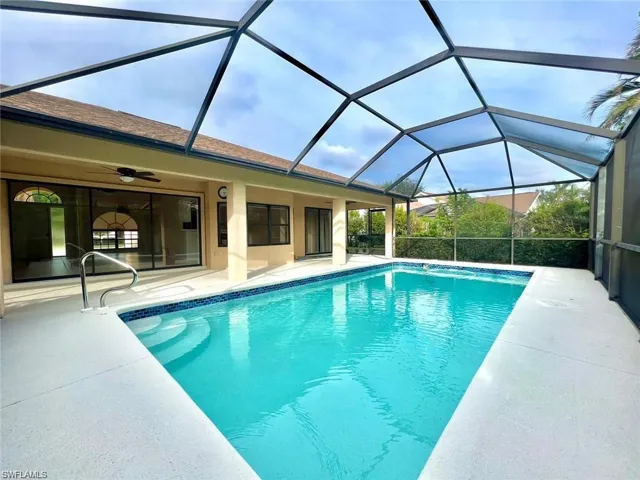 View of pool featuring glass enclosure, ceiling fan, and a patio area