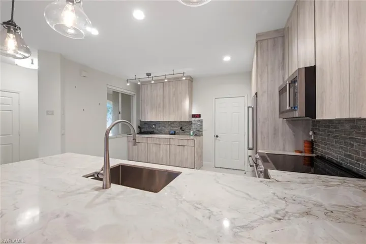 Kitchen with appliances with stainless steel finishes, backsplash, light brown cabinetry, pendant lighting, and sink