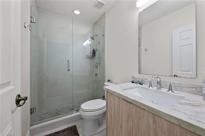 Bathroom with toilet, a shower with door, vanity, and tile patterned flooring