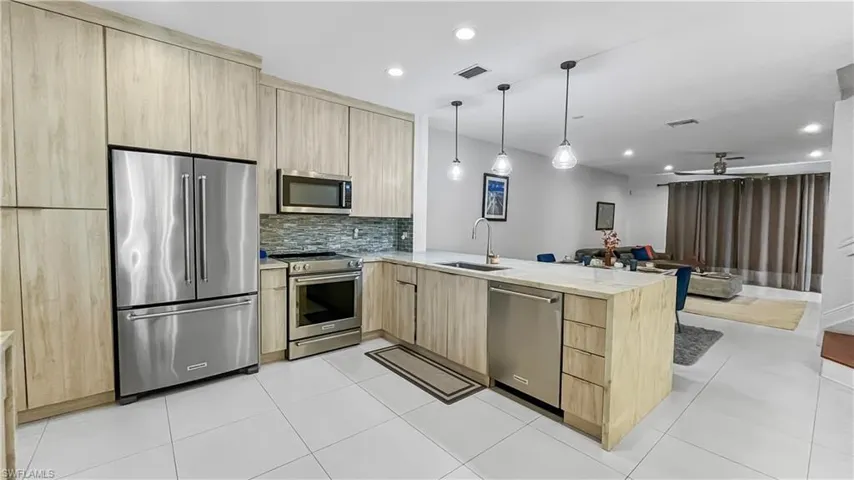 Kitchen featuring stainless steel appliances, light brown cabinetry, sink, kitchen peninsula, and ceiling fan
