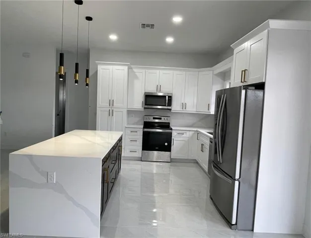 Kitchen with hanging light fixtures, stainless steel appliances, light tile patterned floors, and white cabinets