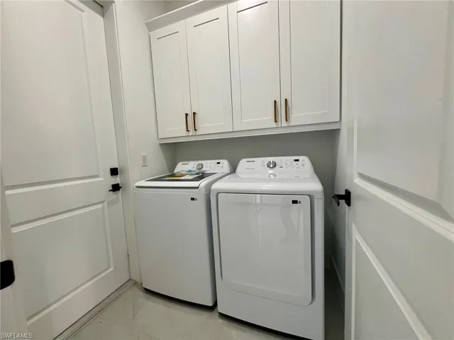 Washroom with light tile patterned flooring, washer and dryer, and cabinets