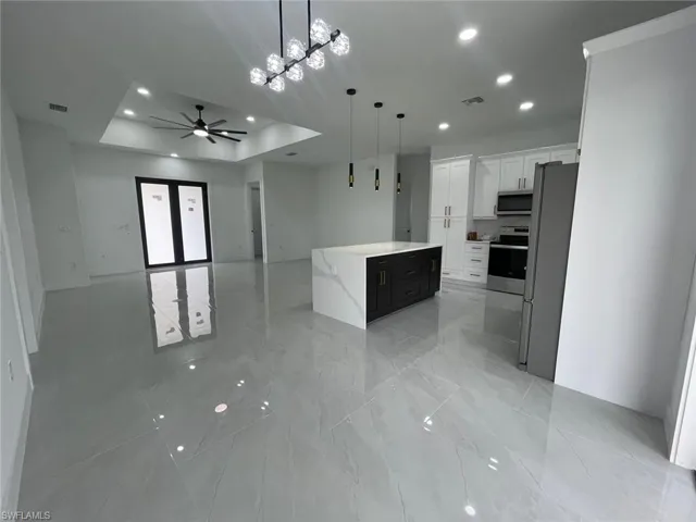Kitchen with a tray ceiling, pendant lighting, white cabinets, a kitchen island, and appliances with stainless steel finishes