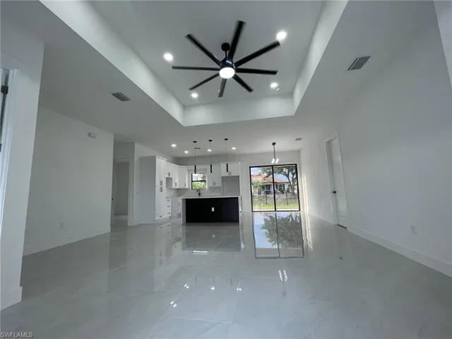 Unfurnished living room featuring light tile patterned flooring, ceiling fan, and a raised ceiling