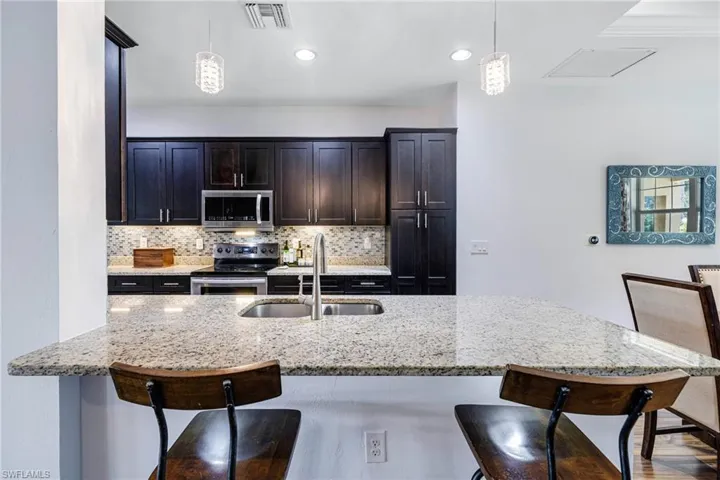 Kitchen with a breakfast bar, sink, hanging light fixtures, light stone counters, and stainless steel appliances