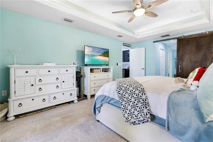 Bedroom with a raised ceiling, ceiling fan, and light colored carpet