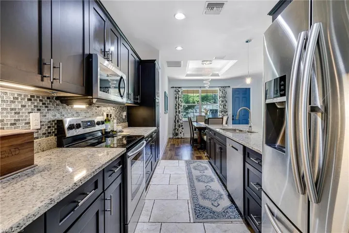 Kitchen featuring light stone countertops, tasteful backsplash, stainless steel appliances, a tray ceiling, and hanging light fixtures