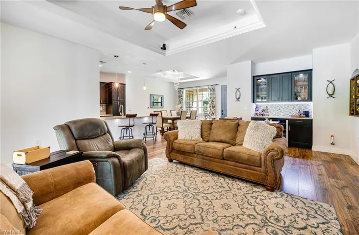 Living room featuring hardwood / wood-style floors, bar area, a raised ceiling, crown molding, and ceiling fan