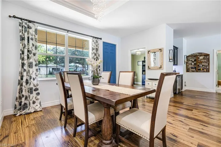 Dining area with ornamental molding, dark wood-type flooring, beverage cooler, and a notable chandelier