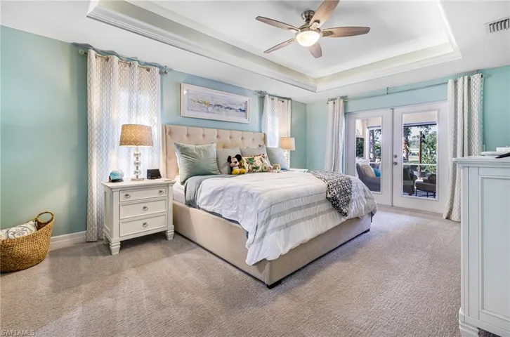 Bedroom featuring french doors, access to outside, a tray ceiling, ceiling fan, and light colored carpet