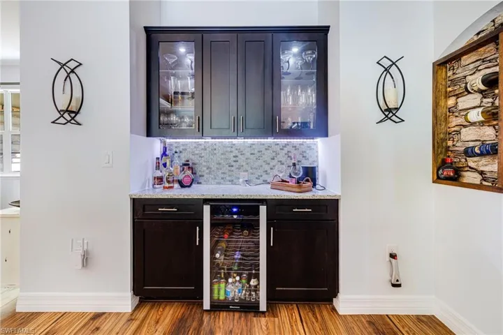 Bar featuring light stone counters, wood-type flooring, beverage cooler, and tasteful backsplash