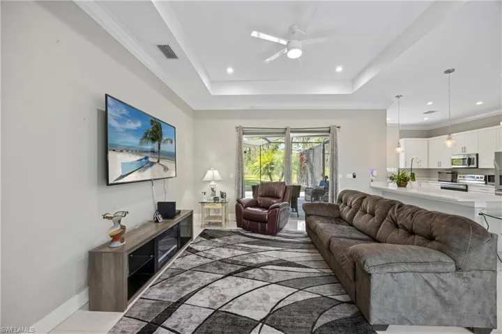 Living area featuring crown molding, a ceiling fan, a tray ceiling, recessed lighting, and light tile patterned flooring