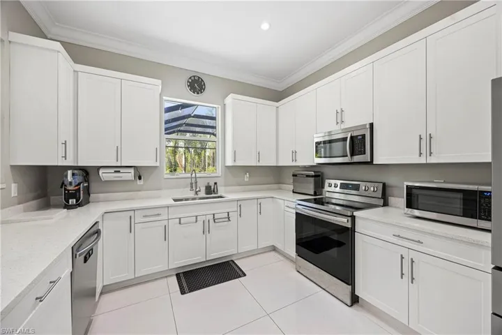 Kitchen featuring stainless steel appliances, crown molding, white cabinets, light tile patterned floors, and recessed lighting