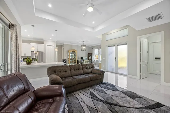 Living room with a tray ceiling, ornamental molding, recessed lighting, light tile patterned floors, and a ceiling fan