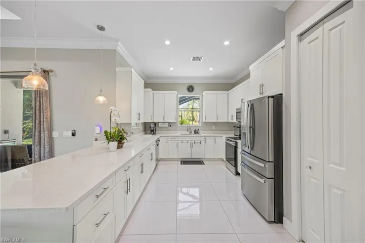 Kitchen featuring white cabinets, stainless steel appliances, ornamental molding, light stone countertops, and decorative light fixtures