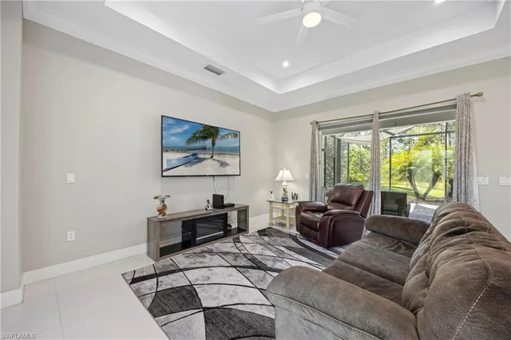 Living area with a raised ceiling, light tile patterned floors, crown molding, recessed lighting, and ceiling fan