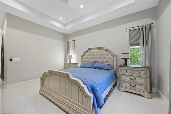 Bedroom with a raised ceiling, ceiling fan, light tile patterned flooring, and recessed lighting