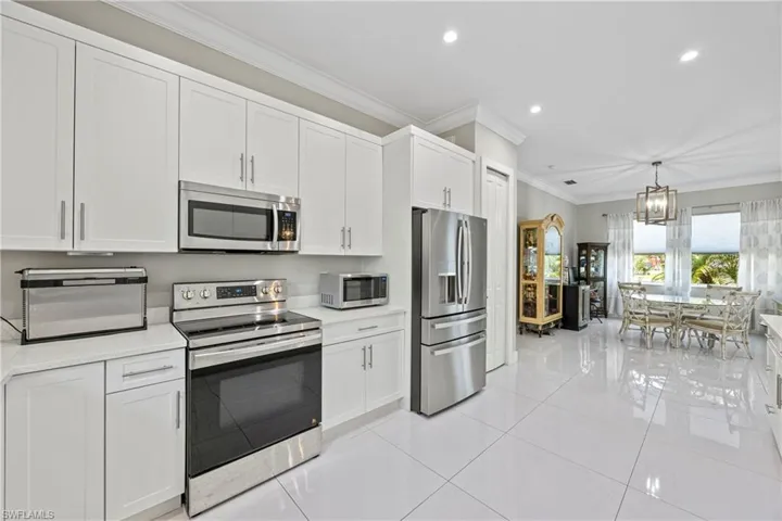 Kitchen featuring crown molding, stainless steel appliances, white cabinets, decorative light fixtures, and light tile patterned flooring