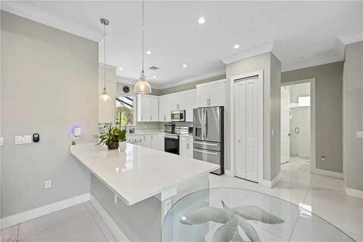 Kitchen with hanging light fixtures, stainless steel appliances, white cabinets, a peninsula, and light stone countertops