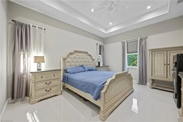 Bedroom featuring light tile patterned floors, a ceiling fan, a raised ceiling, recessed lighting, and freestanding refrigerator