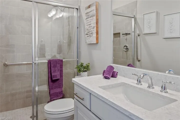 Spacious primary bedroom featuring bay windows, a double tray ceiling with elegant crown molding, recessed lighting, and a modern ceiling fan. Natural light floods the room through a wall of expansive windows, offering serene views and a bright, airy ambiance. Beautiful wood-look tile flooring adds warmth and style, while the wall-mounted TV makes this retreat both functional and relaxing.